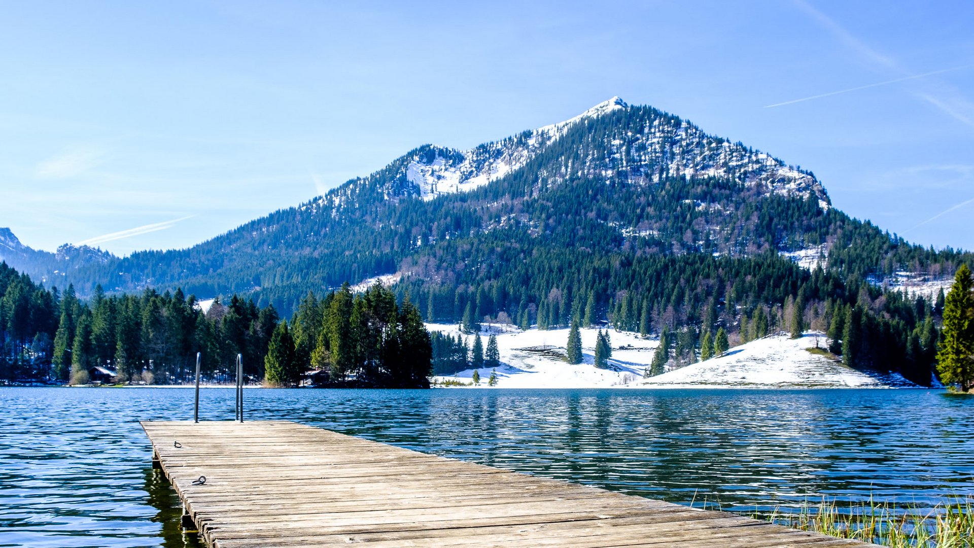Euer authentischer Urlaub am Spitzingsee Holzsteg auf einem Bergsee mit schneebedeckten Gipfeln im Hintergrund