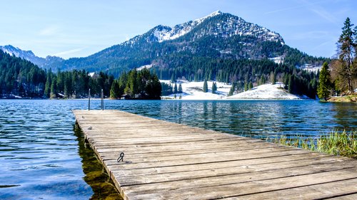 Euer authentischer Urlaub am Spitzingsee Holzsteg auf einem Bergsee mit schneebedeckten Gipfeln im Hintergrund