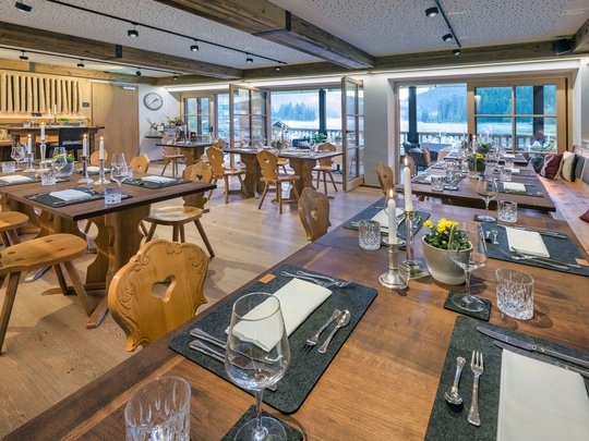 Ein Hotel mit Sauna am See? Ab in die Alte Wurzhütte! Gemütlich gedeckte Holztische in einem gut beleuchteten Restaurant mit Ausblick auf Berge