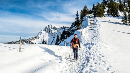 Euer authentischer Urlaub am Spitzingsee Frau wandert auf schneebedecktem Bergweg mit Bergen und Bäumen im Hintergrund