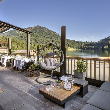 Ein Blick in die Alte Wurzhütte Gemütliche Terrasse mit Seeblick, Hängesessel und Tischen vor Bergkulisse
