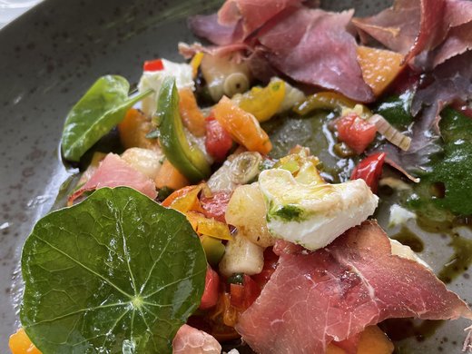 Die Verpflegung bei Tagungen Bunte Vorspeise mit Schinken, Gemüse, Blattsalat und Käse auf grauem Teller