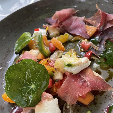 Ein Blick in die Alte Wurzhütte Bunte Vorspeise mit Schinken, Gemüse, Blattsalat und Käse auf grauem Teller