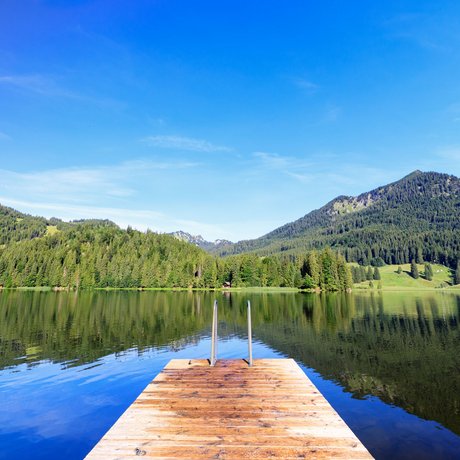 Ein Blick in die Alte Wurzhütte Steg an einem ruhigen See mit Bergblick und klarem Himmel