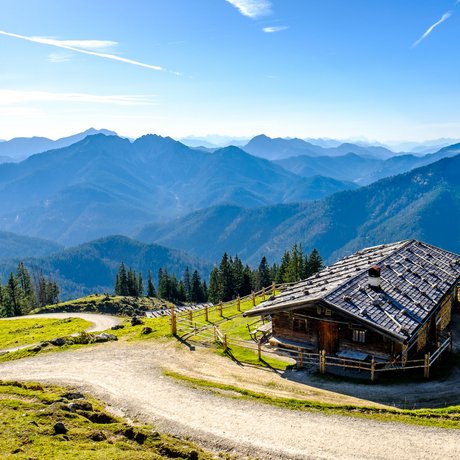 Ein Blick in die Alte Wurzhütte Almhütte mit Bergpanorama und geschwungenem Wanderweg bei klarem Himmel