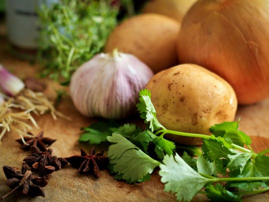 Das perfekte Menü für eure Feier Kartoffeln, Zwiebeln, Knoblauch, Sternanis und frische Kräuter auf Schneidebrett