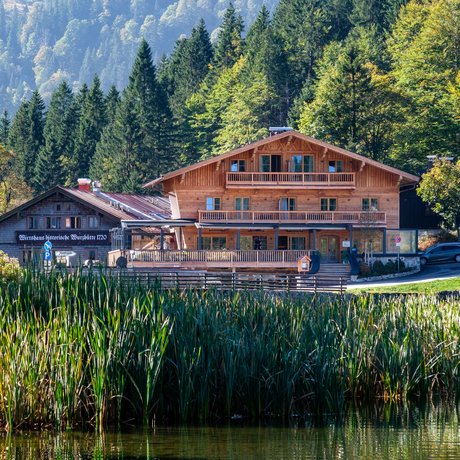 Ein Blick in die Alte Wurzhütte Holzhaus am See mit Bergen und Wald im Hintergrund