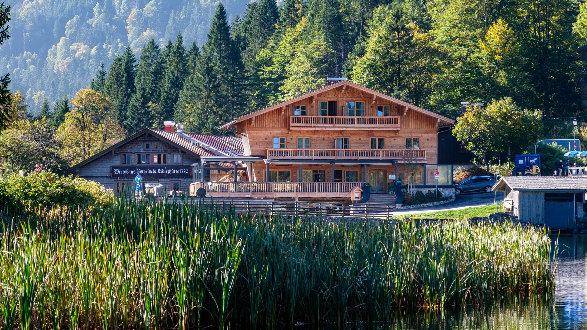 So gelangt ihr zur Alten Wurzhütte. Holzhaus am See mit Bergen und Wald im Hintergrund