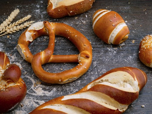 Willkommen im Tagungshotel in Oberbayern! Verschiedene Laugengebäcke auf Holzuntergrund mit Weizenähren und Mehl