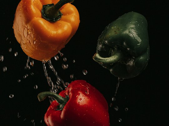 Das perfekte Menü für eure Feier Gelbe, grüne und rote Paprika mit Wassertropfen vor schwarzem Hintergrund