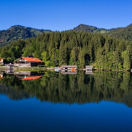 Ein Blick in die Alte Wurzhütte Spiegelung von Häusern und Bäumen in einem ruhigen Bergsee bei klarem Himmel