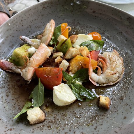 Ein Blick in die Alte Wurzhütte Garnelensalat mit Tomaten, Mozzarella, Basilikum und Croutons auf einem grauen Teller