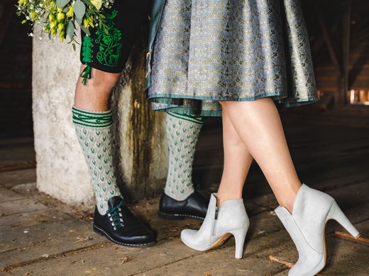 Feiert eure Hochzeit am See! Hände haltendes Paar in traditioneller bayerischer Tracht mit Blumenstrauß