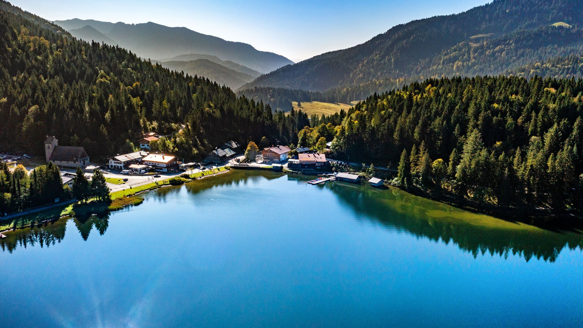 Geburtstag feiern am See? Das ist die perfekte Location. Blick auf einen ruhigen Bergsee umgeben von Wald und Bergen bei klarem Wetter