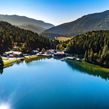 Ein Blick in die Alte Wurzhütte Blick auf einen ruhigen Bergsee umgeben von Wald und Bergen bei klarem Wetter