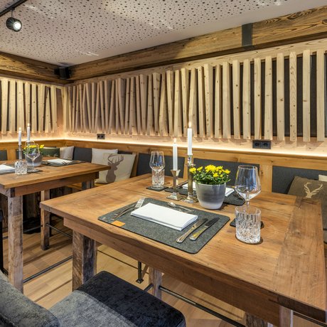 Ein Blick in die Alte Wurzhütte Gemütliche rustikale Essbereiche mit Holztischen und dekorativen Kissen mit Hirschmotiv