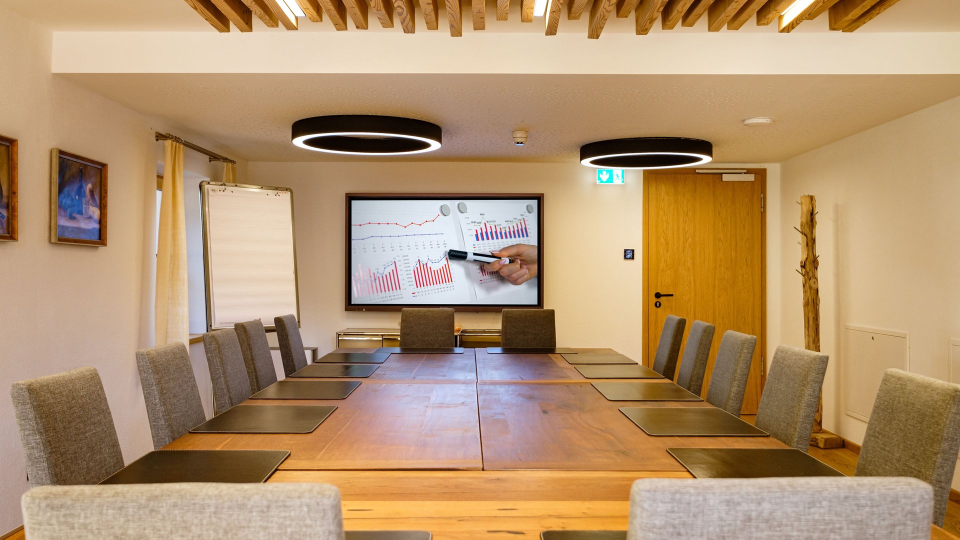 Willkommen im Tagungshotel in Oberbayern! Moderner Konferenzraum mit großem Holztisch und Präsentationsbildschirm