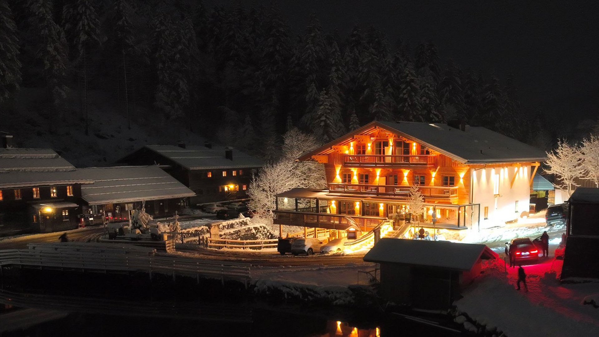 Ein Hotel mit Sauna am See? Ab in die Alte Wurzhütte! Beleuchtetes Haus und schneebedeckte Landschaft bei Nacht mit Autos und Bäumen