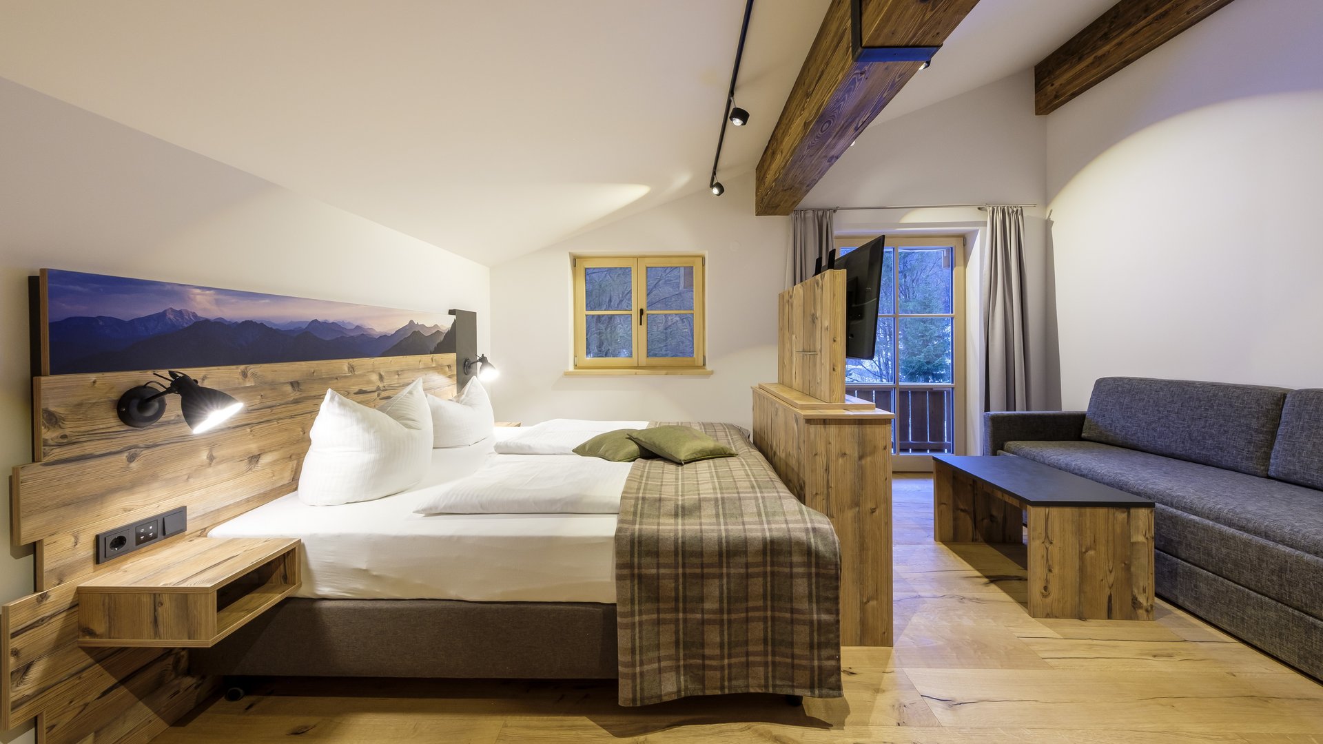 Mit einem Lächeln aufstehen im Hotel am Spitzingsee Gemütliches Hotelzimmer mit Holzmöbeln, Doppelbett, Sofa und Balkon