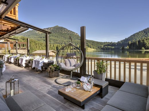 Eating at our restaurant at Lake Spitzingsee Cozy terrace with lake view, hanging chair and dining tables against mountain backdrop