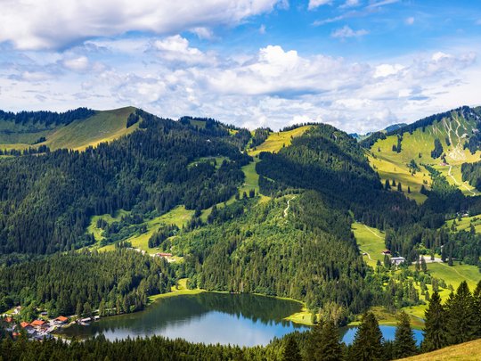 Mit einem Lächeln aufstehen im Hotel am Spitzingsee Bergsee umgeben von Wäldern und grünen Hügeln unter blauem Himmel