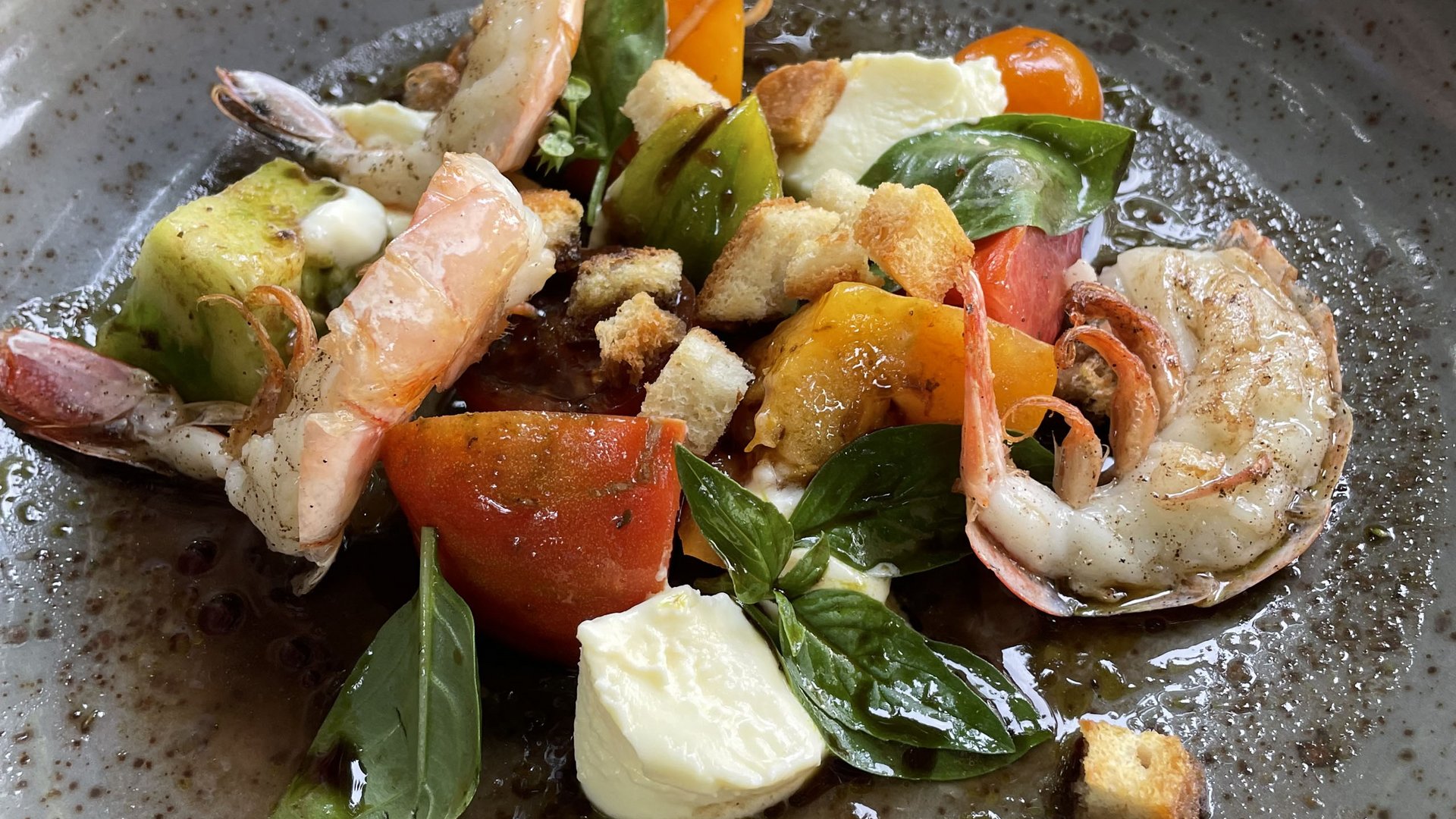Eating at our restaurant at Lake Spitzingsee Shrimp salad with tomatoes, mozzarella, basil, and croutons on a gray plate