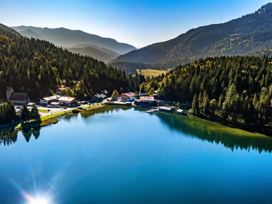 Mit einem Lächeln aufstehen im Hotel am Spitzingsee Blick auf einen ruhigen Bergsee umgeben von Wald und Bergen bei klarem Wetter