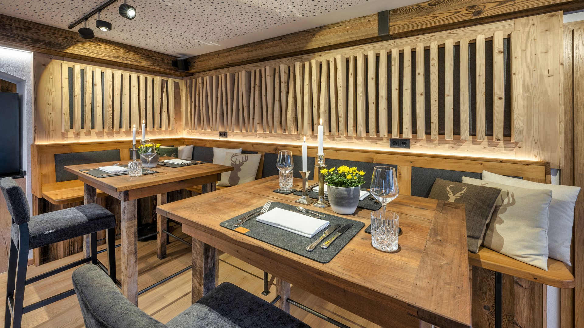 Mit einem Lächeln aufstehen im Hotel am Spitzingsee Gemütliche rustikale Essbereiche mit Holztischen und dekorativen Kissen mit Hirschmotiv